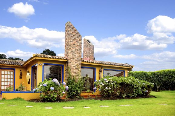 Buntes Haus mit Steinmauer, umgeben von Garten und blauem Himmel.